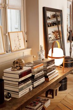 there is a table with many books on it and a lamp next to the window