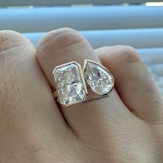 a person's hand holding a ring with two diamonds on it and the middle one is