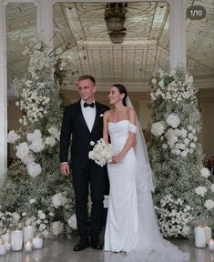 a man and woman standing next to each other in front of white flowers on display