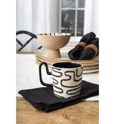 a black and white coffee cup sitting on top of a wooden table next to plates