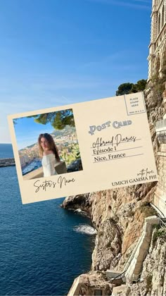 an old postcard is hanging on the side of a cliff by the ocean with a woman's face