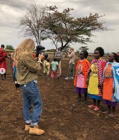 a group of people standing on top of a dirt field next to each other in front of a tree