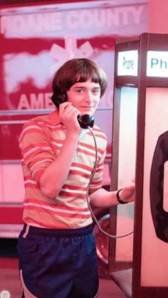 a young man standing in front of a pay phone booth while talking on the phone