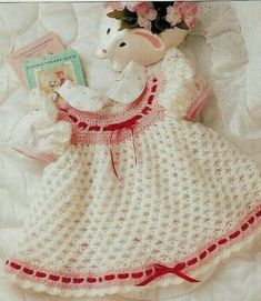 a crocheted baby dress and teddy bear are laying on a white blanket with pink flowers