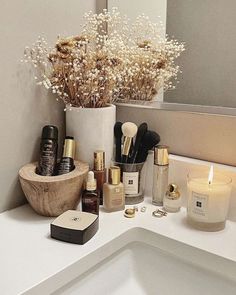 a bathroom counter with various beauty products and flowers in a vase next to the sink