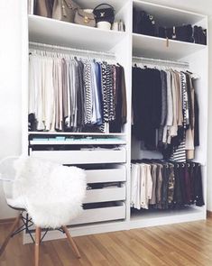 a white closet filled with lots of clothes and bags on top of shelves next to a chair