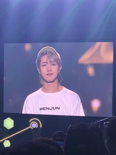 a person on a stage with a video screen in front of them that says renjun