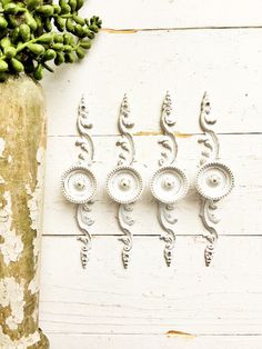 four metal wall hangings on the side of a white wooden wall next to a vase with green flowers