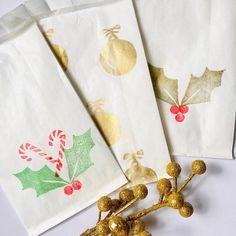 three christmas napkins with holly and gold decorations on them, sitting next to each other