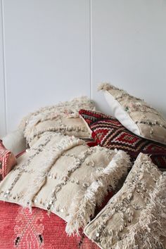 a pile of pillows sitting on top of a red rug next to a white wall