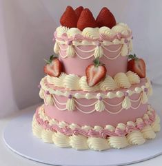 a three tiered pink cake with strawberries on top and white icing around the edges