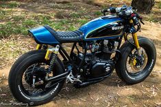 a blue and black motorcycle parked on top of a dirt field next to a tree