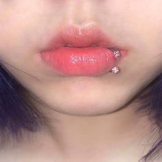 a woman with purple hair and piercings on her lip is wearing pink lipstick,