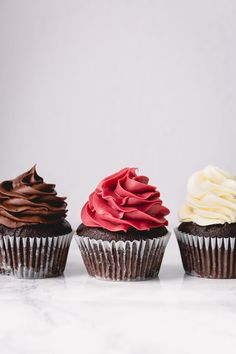 three cupcakes with chocolate frosting and red icing on them sitting next to each other