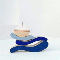 a wooden sailboat sitting on top of a blue and white wave shaped object with a red sail