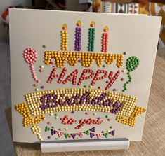 a happy birthday card with candles and beads on the front, sitting on a table