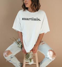 a woman sitting on a stool with flowers in her hand and wearing a t - shirt that says martinis