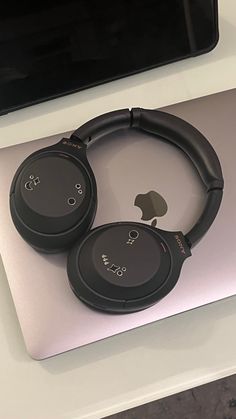 two black headphones sitting on top of an apple laptop computer next to each other