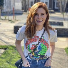 a woman standing on the sidewalk with her hands in her pockets and smiling at the camera