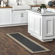 a kitchen with white cabinets and wood flooring is pictured in this image, there is a rug on the floor next to the sink