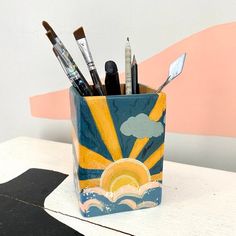 a cup filled with lots of different types of paint and brushes on top of a table