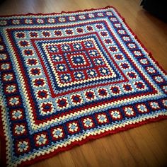 a red, white and blue crocheted afghan on the floor with wood floors