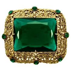 Gold plated filigree brooch featuring a large emerald green glass stone and eight green accent stones. Measuring length 5.4 cm / 2.1 inches by width 4.7 cm / 1.8 inch. This is a beautiful and elegant statement brooch with emerald green glass stones. Circa 1960s. Antique Green Brooch For Evening, Elegant Green Filigree Brooches, Green Brooch Jewelry For Evening, Vintage Green Brooch Jewelry, Vintage Green Brooch For Evening, Green Evening Brooch Jewelry, Ornate Green Jewelry For Evening, Art Deco Green Brooches For Wedding, Ornate Green Brooches For Wedding