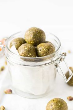 a glass jar filled with green balls next to nuts