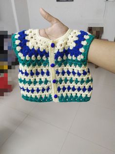 a hand holding up a crocheted sweater with blue and white stars on it