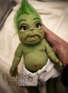 a baby doll with green hair is being held up by someone's hand,