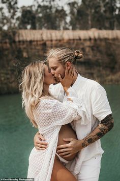 a man and woman kissing in front of water