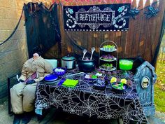 a man sitting at a table with halloween decorations on it, in front of a wooden fence