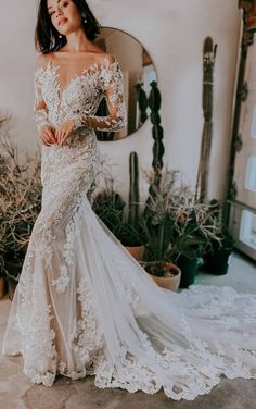 a woman standing in front of a mirror wearing an off the shoulder white wedding dress