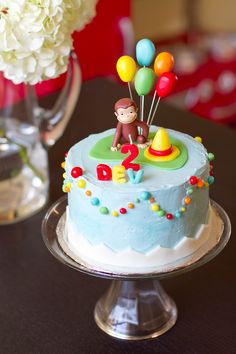 a blue birthday cake with balloons and a monkey on top is sitting on a table