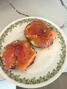 two pieces of bread with salmon and onions on them sitting on a green and white plate