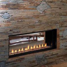 a fire place in the middle of a living room with wood flooring and stone walls