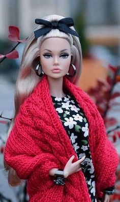 a barbie doll wearing a red cardigan and black floral print dress standing in front of a tree