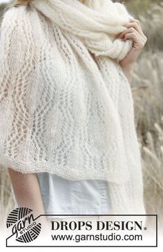 a woman wearing a white knitted shawl in front of some tall dry grass