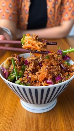 a woman is holding chopsticks over a bowl of food on a wooden table