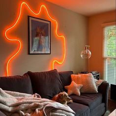 a dog laying on top of a brown couch under a neon orange light in a living room