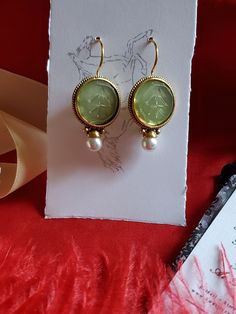 I saw these earrings and knew they were perfect to offer in the shop.  They are gold plated earwires with a round glass green intaglio and pearl drop.  Perfect to wear for late 18th century, early 19th century on up to today.  I love them! They measure 1-1/4 inches long by 3/4 inch wide.  The earwire is super long which is good to stay in the ear. Lots of inspiration on my Pinterest page.  https://www.pinterest.com/kkwalte/_saved/ Yellow Gold Round Earrings With Intaglio, Yellow Gold Round Intaglio Earrings, Gold Byzantine Pierced Earrings, Antique Dangle Earrings As Gift, Brass Pearl Earrings With Ear Wire As Gift, Antique Gold Pearl Earrings, Antique Gold Pearl Earrings As Gift, Gold Pearl Earrings With Lever Back For Gift, Victorian Drop Earrings With French Hook