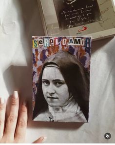 a woman's hand holding up a book with the cover pulled back to show her face