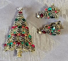 "Vintage Christmas trees, Pakula, Weiss, Seasonal Jewelry, Holiday pins, pins brooches, Eisenberg, Warner BOOK PIECE ~ Page 120 \"O Christmas Tree Book\" This PAKULA rope loop design Christmas tree brooch includes 15 medium-sized red and green rhinestones. The matching clip earrings have the coordinating color rhinestones. Measures 2 1/2\" tall x 1 1/2\" wide. The matching earrings are 1\" tall. All 3 pieces are signed PAKULA on the reverse. A beautiful set in very good vintage condition. Gift Giving ~ All jewelry items will be presented in a lovely gift box with ribbon. ❤️❤️WELCOME!❤️❤️ Please review my photos and product description before purchasing. If you have any questions PLEASE DON'T HESITATE TO SEND ME A MESSAGE  and I will be more than happy to assist.  I try my best to answer qu Christmas Festive Jewelry With Rhinestones, Festive Holiday Jewelry With Rhinestones, Festive Brooch Jewelry, Traditional Christmas Festive Jewelry, Traditional Festive Christmas Jewelry, Holiday Red Brooch Jewelry, Red Holiday Brooch, Vintage Christmas Brooches, Christmas Tree Red