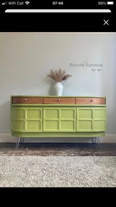 a green dresser with some drawers and a vase on it's top, in front of a white wall