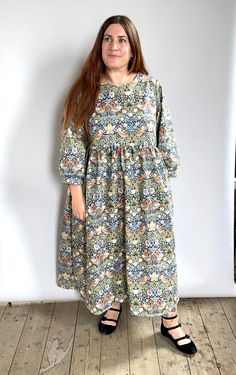 a woman standing in front of a white wall wearing a dress with flowers on it