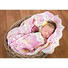 a newborn baby wrapped in a pink and white crochet blanket is laying in a wicker basket