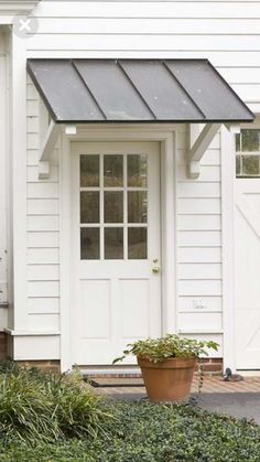 a white house with a large potted plant in front of it and a black awning over the door