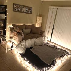 a living room with lights on the floor and a couch covered in blankets, pillows and blankets