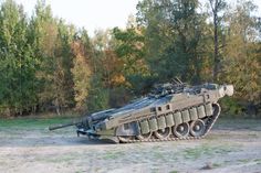 an army tank is sitting in the middle of a dirt field with trees in the background