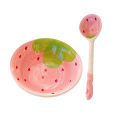 a pink and green bowl next to a plastic spoon on a white surface with red dots